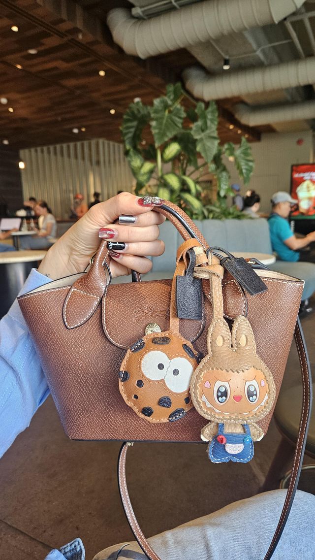 A handcrafted leather bag charm attached to a handbag during a conversation